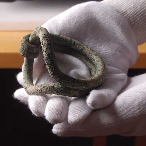 Bronze Age Sussex loop bracelet cradled in the palm of a hand wearing white gloves